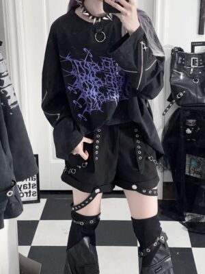 Oversized black jirai kei gothic long-sleeve t-shirt with purple thorn cross print and functional zipper cuff details, worn by model in alternative goth indoor setting with spiked accessories