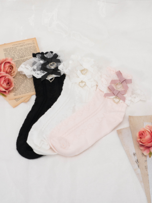 Flat lay collection of three Jirai Kei heart rhinestone lolita mid-calf socks in different colors with lace trim bows displayed on vintage books and artificial roses