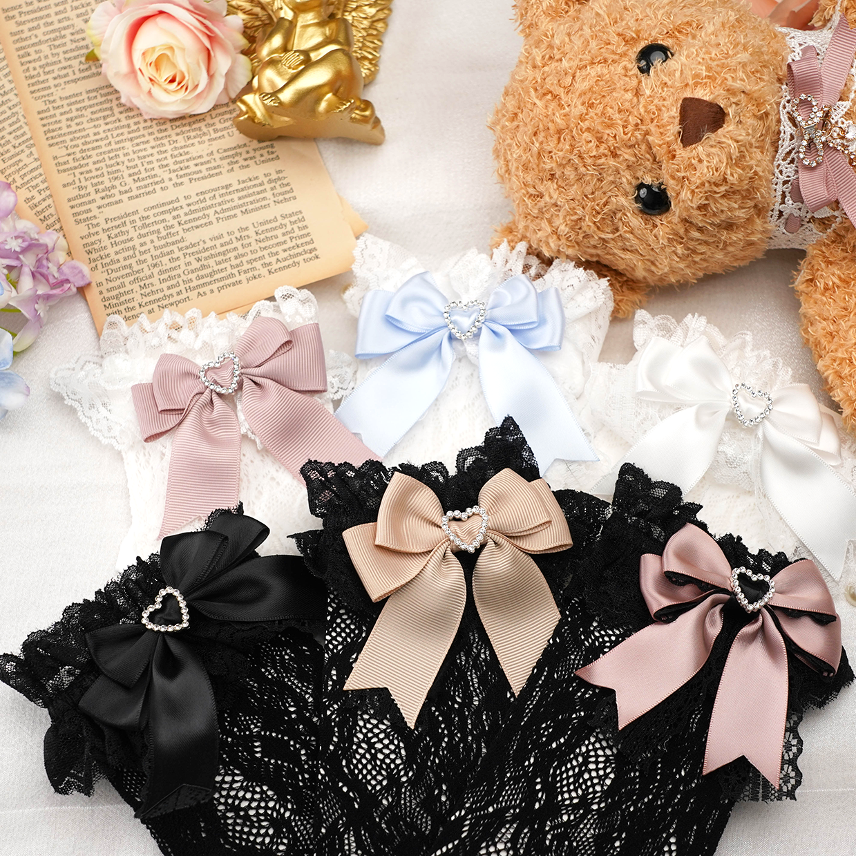 Top-down flat lay of jirai kei lace ankle socks with pastel satin bows and heart rhinestone embellishments styled with teddy bear vintage book and flowers