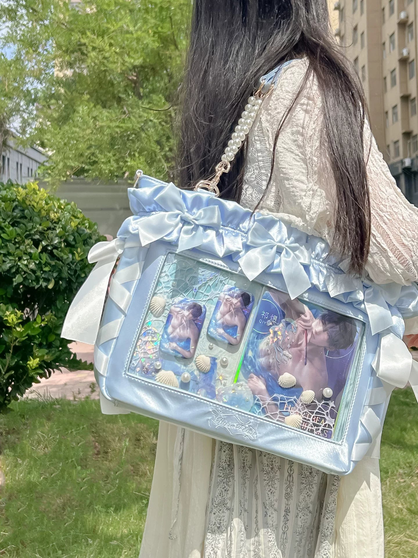 Baby blue Jirai Kei 14 inch laptop itabag back shoulder view satin bow details transparent display with anime prints chain shoulder strap outdoor park setting