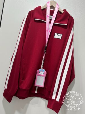 Flat lay display of maroon track jacket with white contrast stripes and embroidered chest name tag, shown on clothing rack with pink lanyard accessory, professional product photography for Japanese subculture fashion