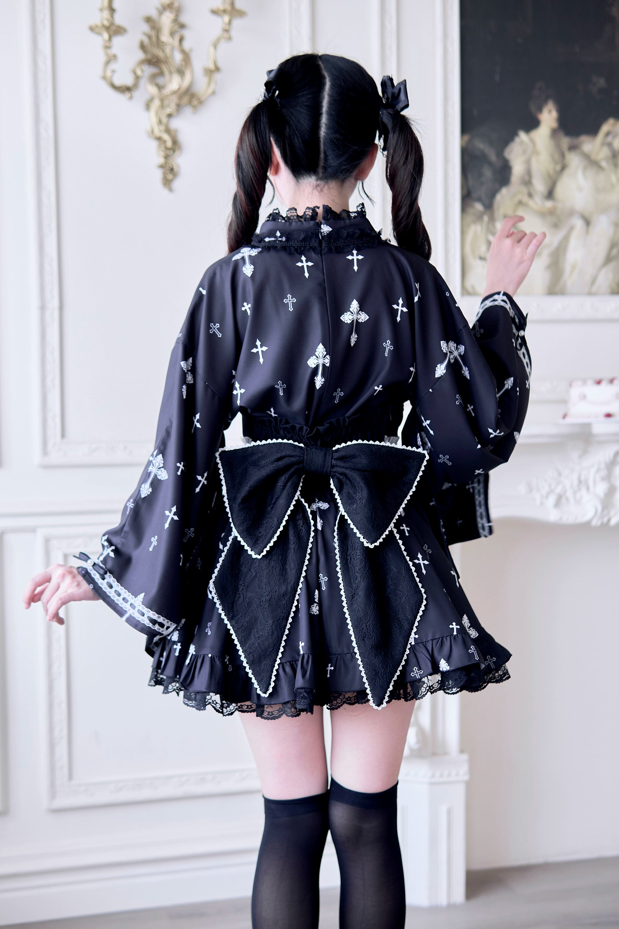 Black Jirai Kei kimono outfit back view featuring dramatic large black bow, cross printed fabric, and ruffled mini skirt hem in vintage parlor setting