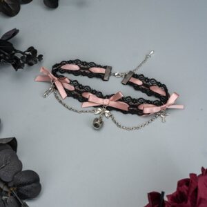 Black and pink Jirai Kei lace choker with double-layer lace dual satin bows and bell pendant chain displayed on grey backdrop with dried dark flowers romantic goth necklace detail