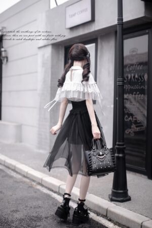 Back three-quarter street view of complete Jirai Kei outfit featuring sheer black tulle overlay skirt, ruffled white cape blouse, platform boots, and studded handbag styled on model