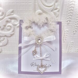 Ivory white heart-shaped tulle hair clip with rhinestone embellishments and white satin bow, product flat lay on display card