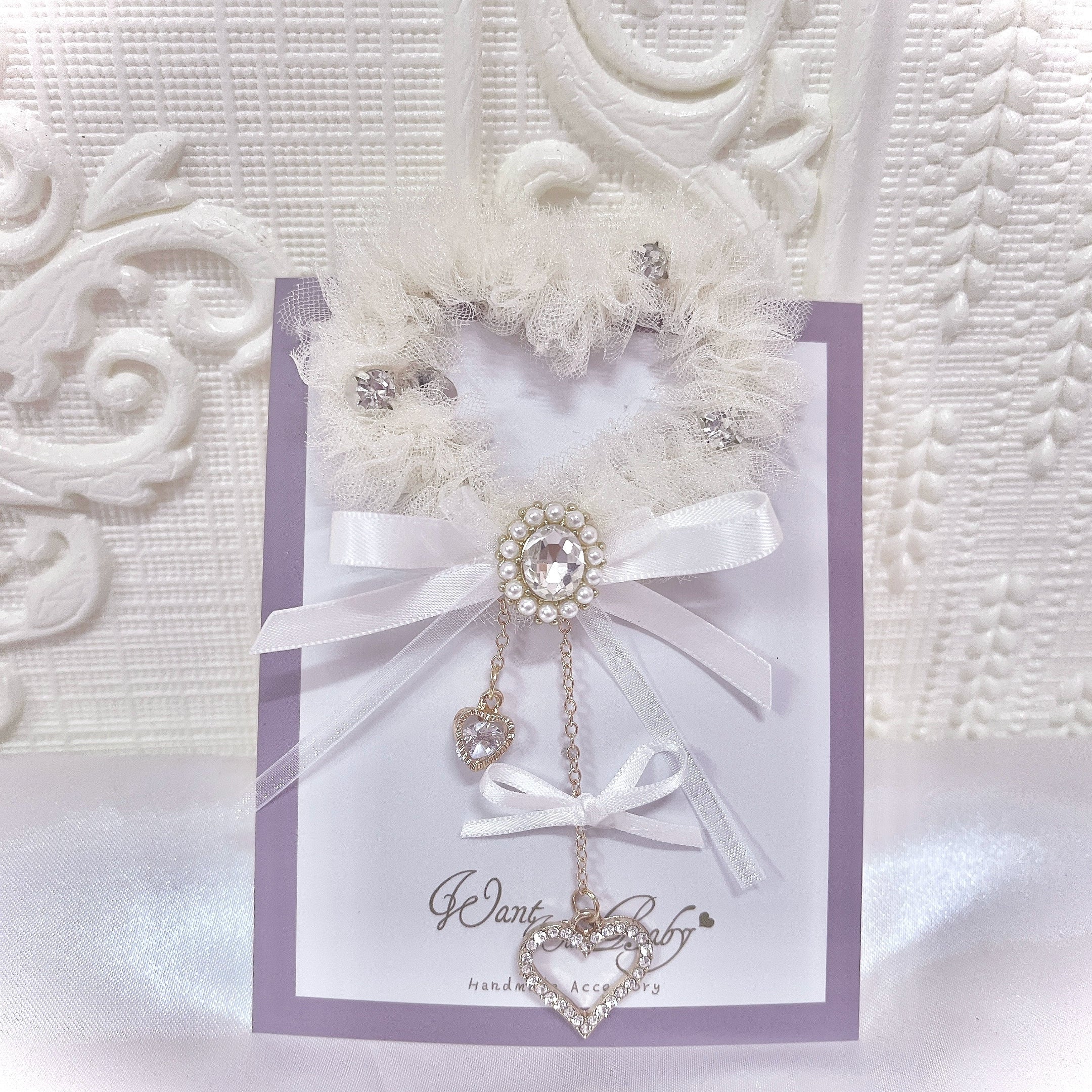 Ivory white heart-shaped tulle hair clip with rhinestone embellishments and white satin bow, product flat lay on display card