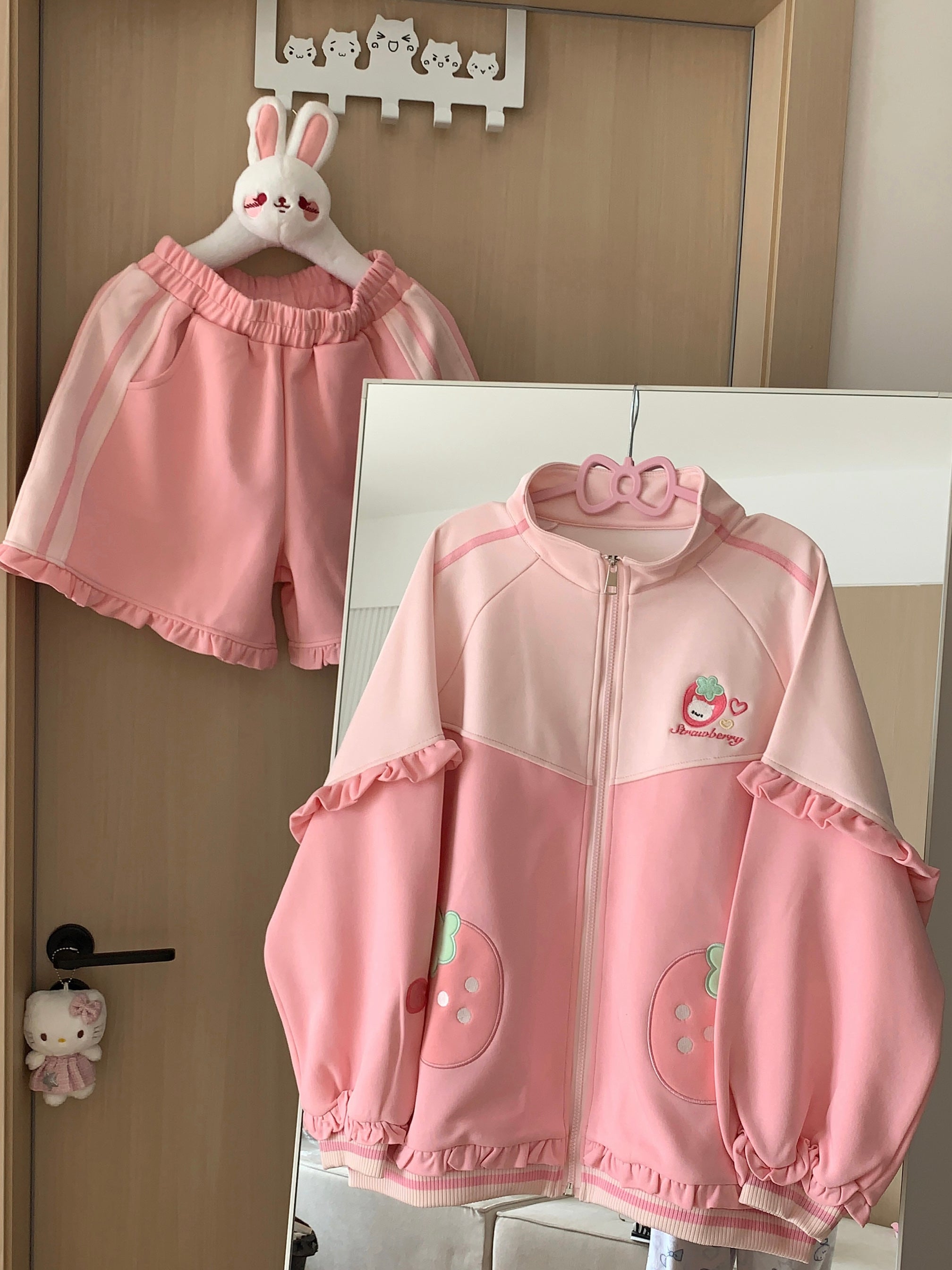 Pink strawberry Jirai Kei two-piece outfit flat lay display, featuring stand collar coat with ruffled edges and strawberry logo embroidery paired with coordinating shorts with bow and heart embroidery details