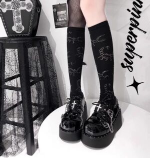 Jirai Kei platform shoes with metal cross buckle worn with patterned knee-high socks, glossy black patent leather finish, front low-angle view