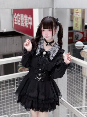 All-black jirai kei two-piece outfit with lace ruffled peter pan collar, tiered lace skirt, heart-shaped waist accessory, model on outdoor Japanese balcony