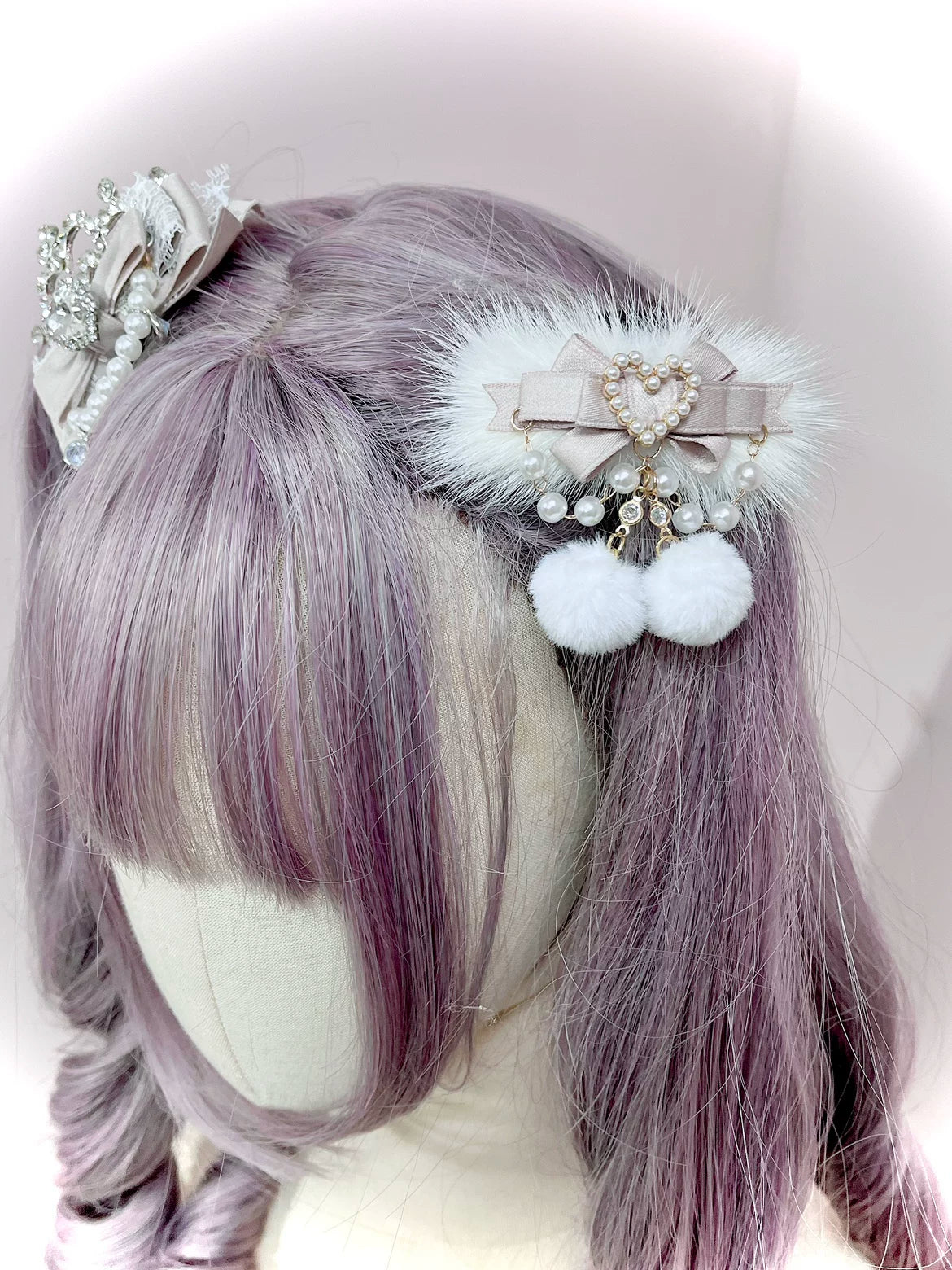 Beige ryousangata pom-pom hair clip with heart pearl charm and white fluffy pom-poms on mannequin head with light purple curly bangs, jirai kei lolita hair accessory left side view