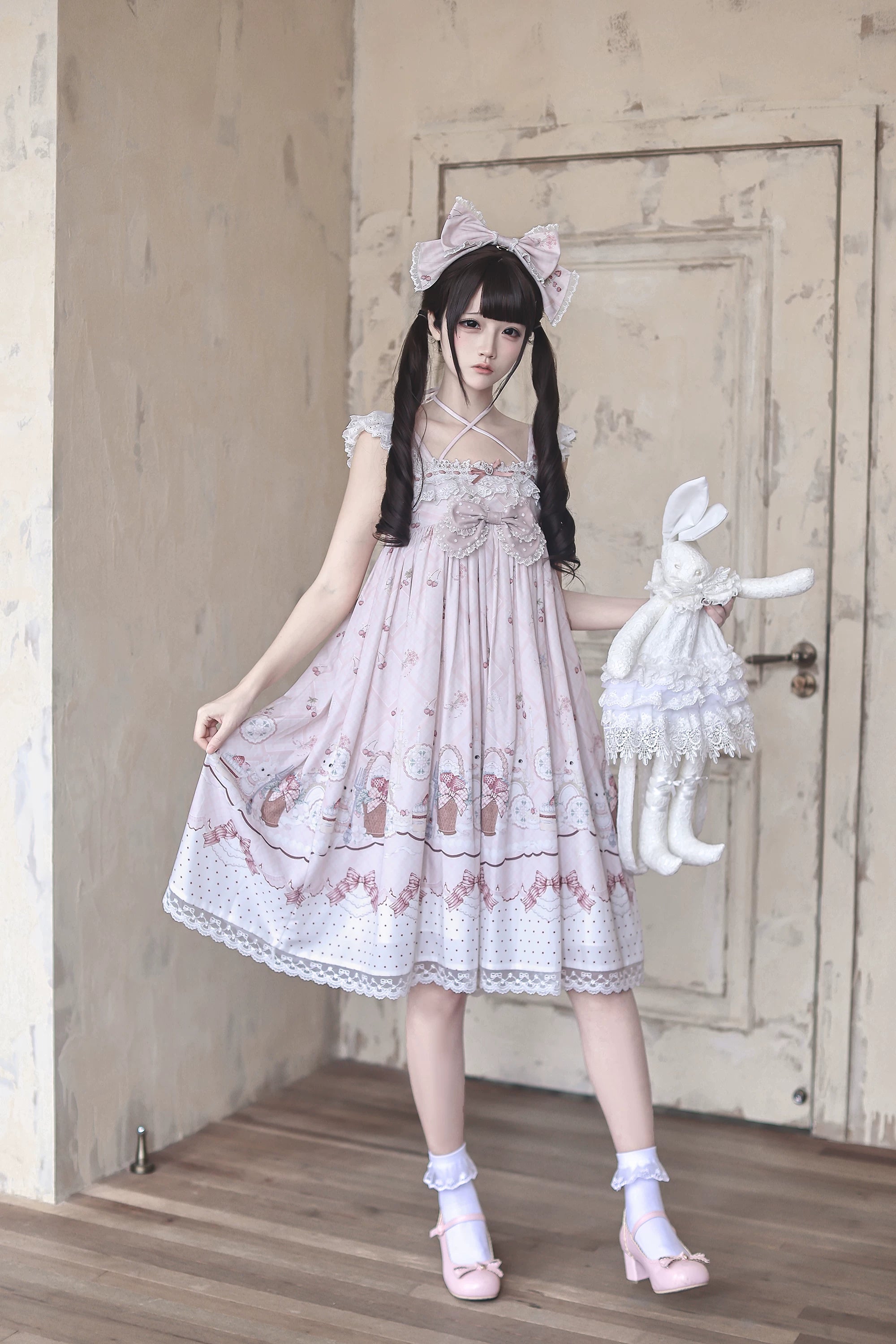 Side-front full-body shot of strawberry bunny Jirai Kei Lolita dress slip style worn by twin-tailed model holding lace rabbit plush with cartoon bunny print visible