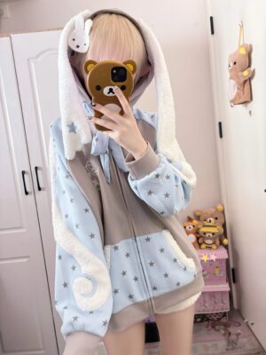 Kawaii angel wing bunny ear zip hoodie front half-body view featuring light blue and gray color block design with star prints and fuzzy trims worn by blonde model