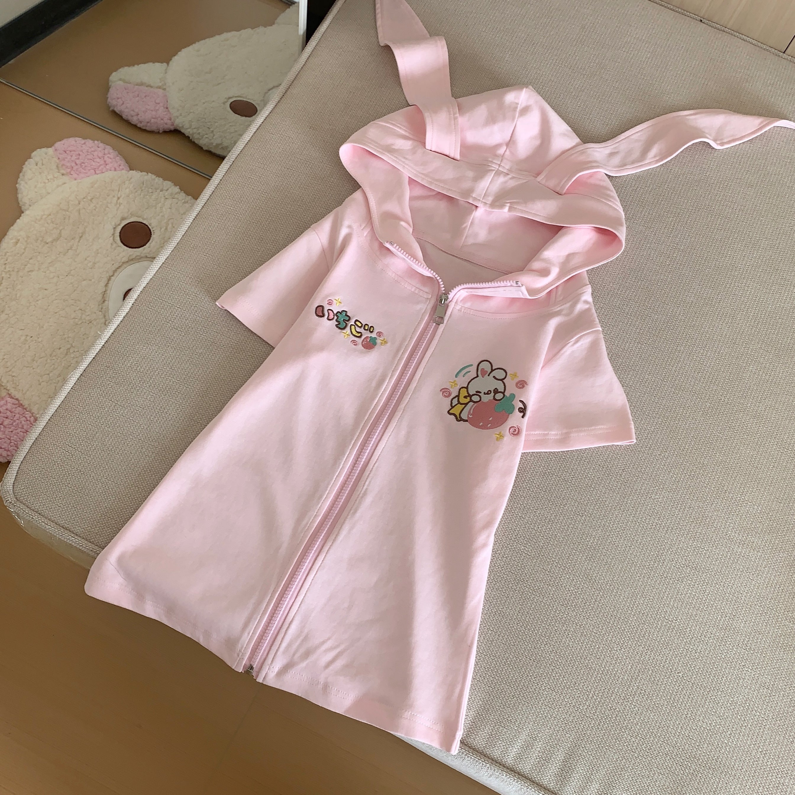 Flat lay top view of pink kawaii bunny-ear zip hoodie showing short sleeves embroidered details and bunny hood design