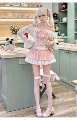 Sweet pink Jirai Kei lolita two-piece outfit set with tiered ruffled skirt, lace bow detail, and fishnet thigh-high socks, full-body front view in retro home kitchen setting