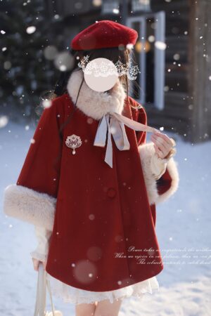 Jirai Kei red wool cape cloak with beige faux fur collar and hand-tied bow, worn by model in snowy outdoor setting with wooden cabin backdrop, front left three-quarter view showing Victorian-inspired silhouette and festive holiday aesthetic