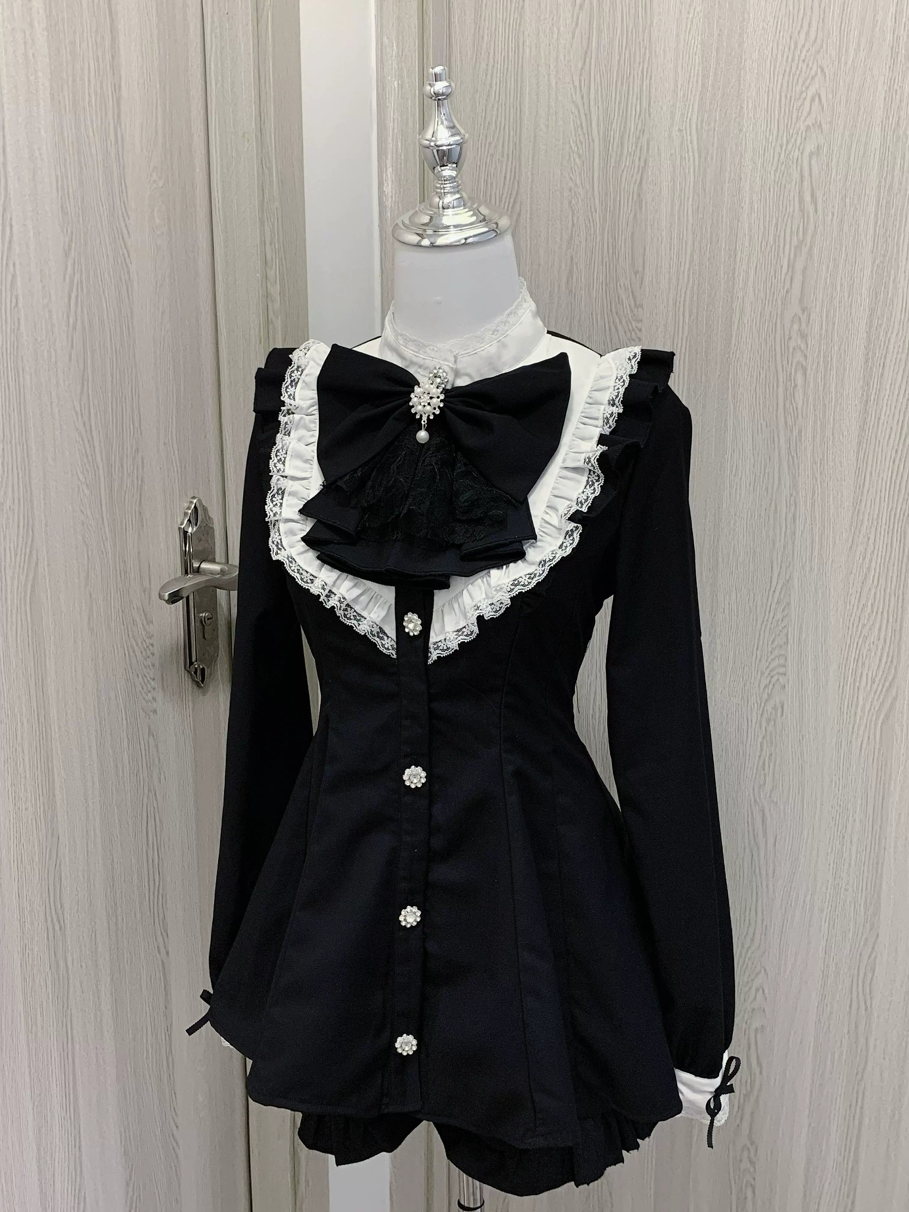 Long sleeve Jirai Kei dress front view on mannequin in black and white color scheme, featuring pearl button front closure and gothic lace bow collar