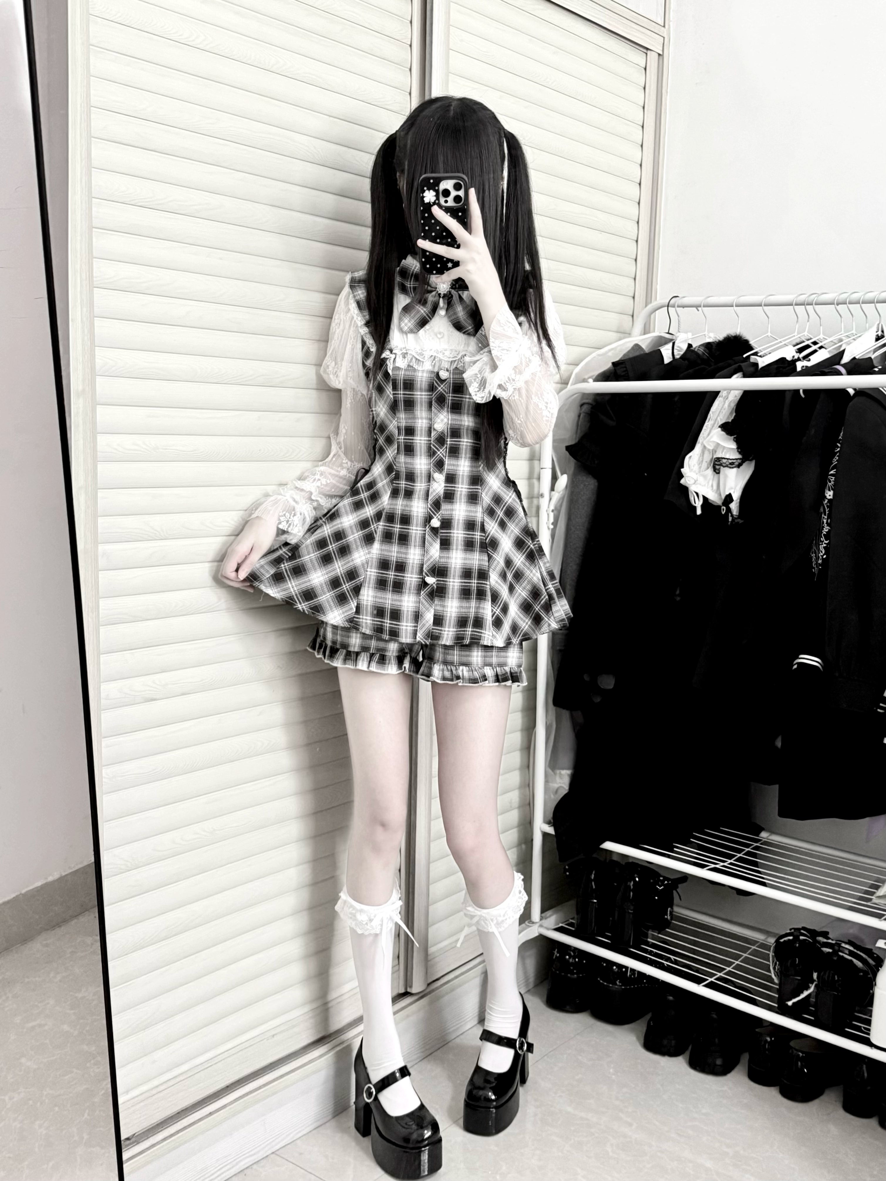Side profile full body view of plaid Jirai Kei romper dress with lace sleeves matching shorts and platform shoes worn by masked female model against clothing rack