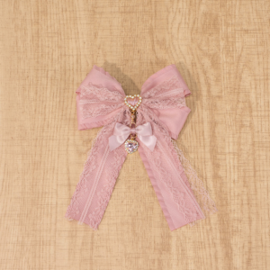 Dusty pink Jirai Kei lace double bow brooch with sparkling rhinestone heart charm, handcrafted satin ribbon detail, flat lay on wooden surface