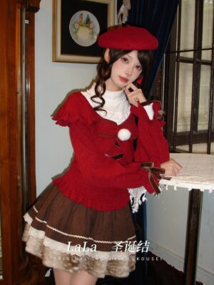 Close-up front view of festive red jirai kei sweater showing white pompom decoration and lace-up design details, coordinated with brown tiered skirt ensemble