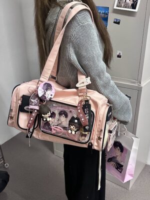 Pink cylinder ita bag worn as shoulder carry on model in grey knit sweater, displaying anime character badges in clear front window with dangling charms
