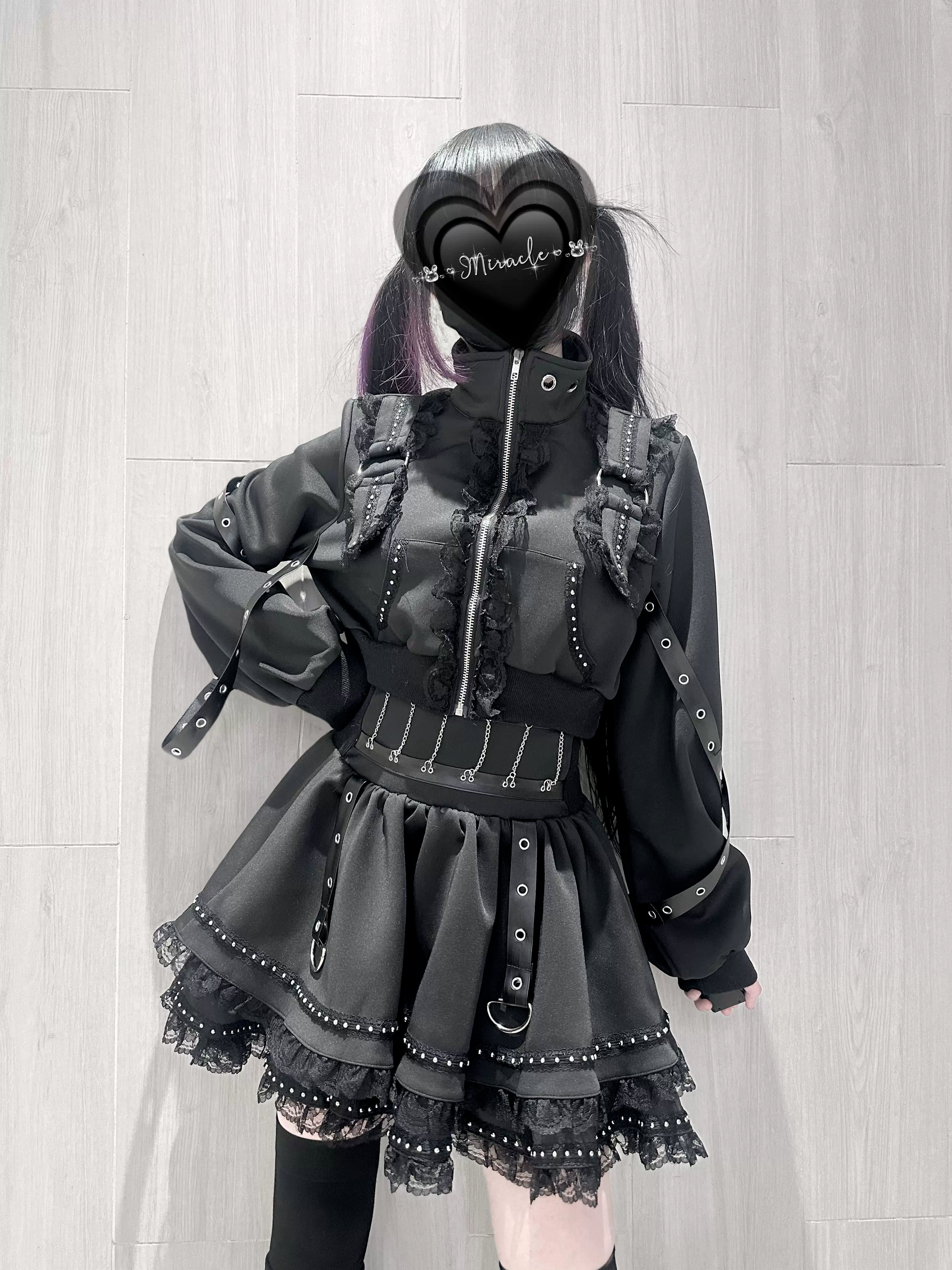 Jirai Kei goth cross-zip jacket and lace mini skirt set with leg warmers front three-quarter view on model with twin tails heart face cover wooden wall background