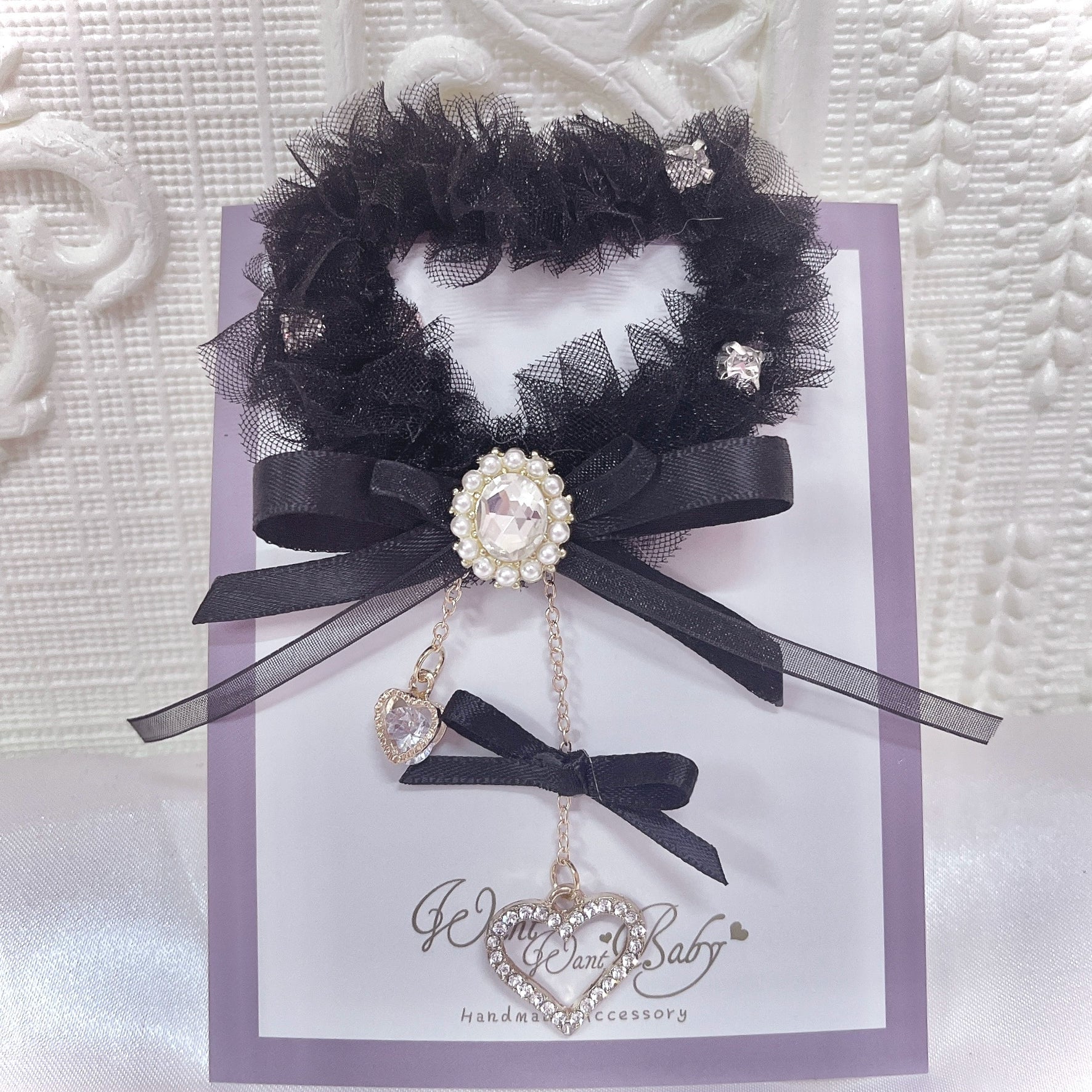 Black heart-shaped tulle hair clip with layered black satin bows and rhinestone details, displayed on branded card