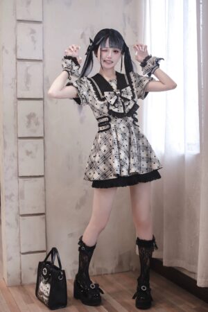 Full front standing view of plaid polka dot Jirai Kei sailor collar lolita dress with oversized black bow and lace-trimmed ruffled hem worn by model in vintage indoor setting