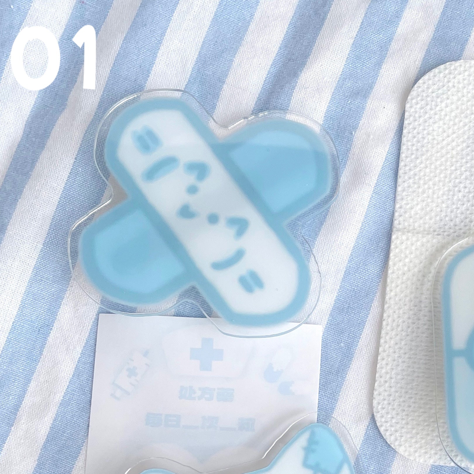 Tenshi Kaiwai cross bandage acrylic hair clip with smiling face design on blue-striped fabric background with medical prescription card