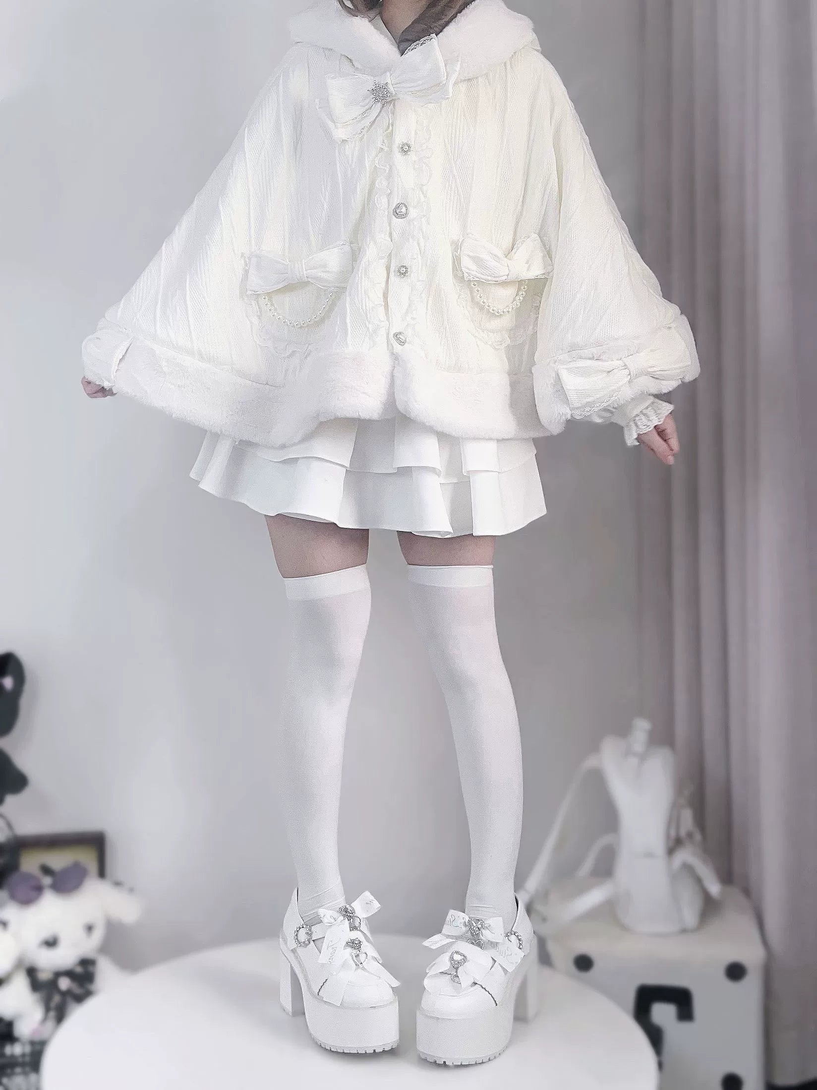 Back mirror selfie view of white fleece cape coat highlighting plush hood trim, batwing sleeves design, and matching white mini skirt
