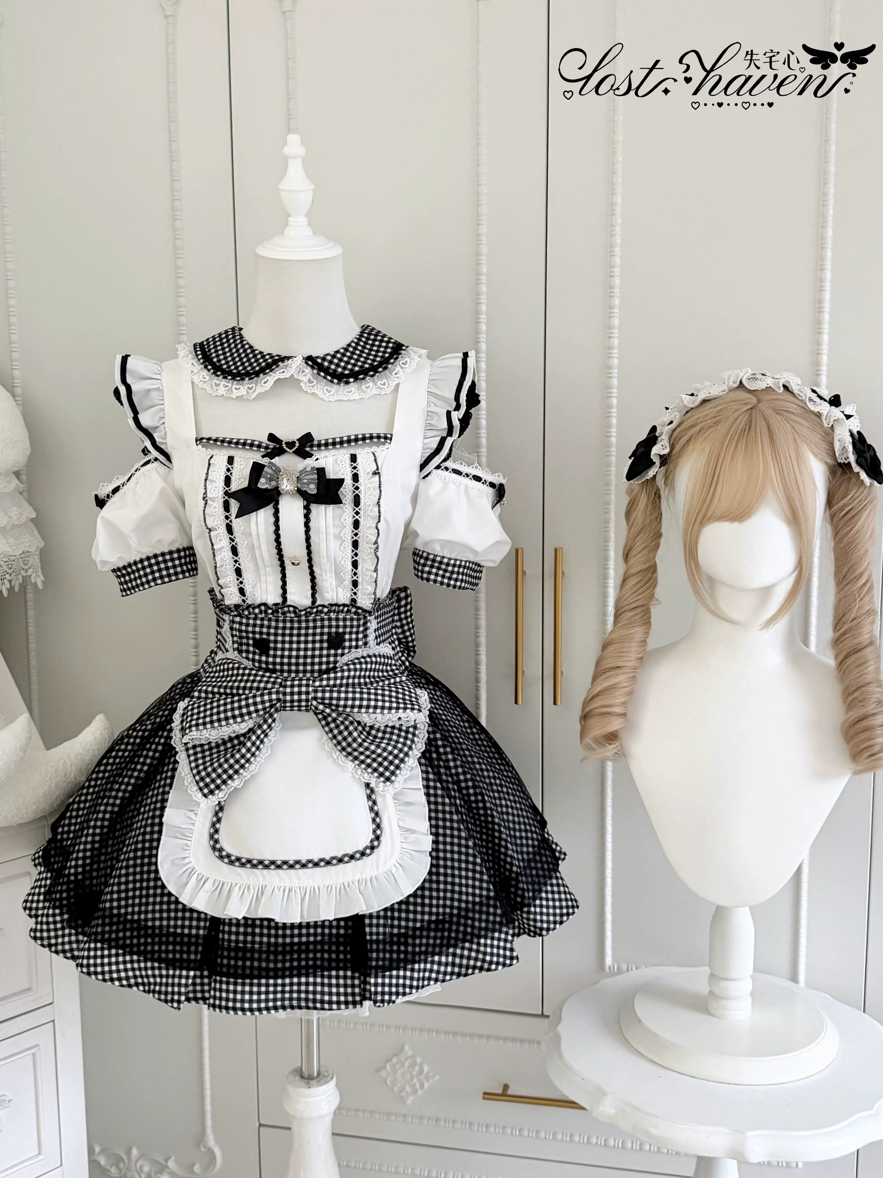 Front display view of black and white gingham Jirai Kei maid dress set with doll collar, ruffled apron hem, and heart button details in luxury closet setting