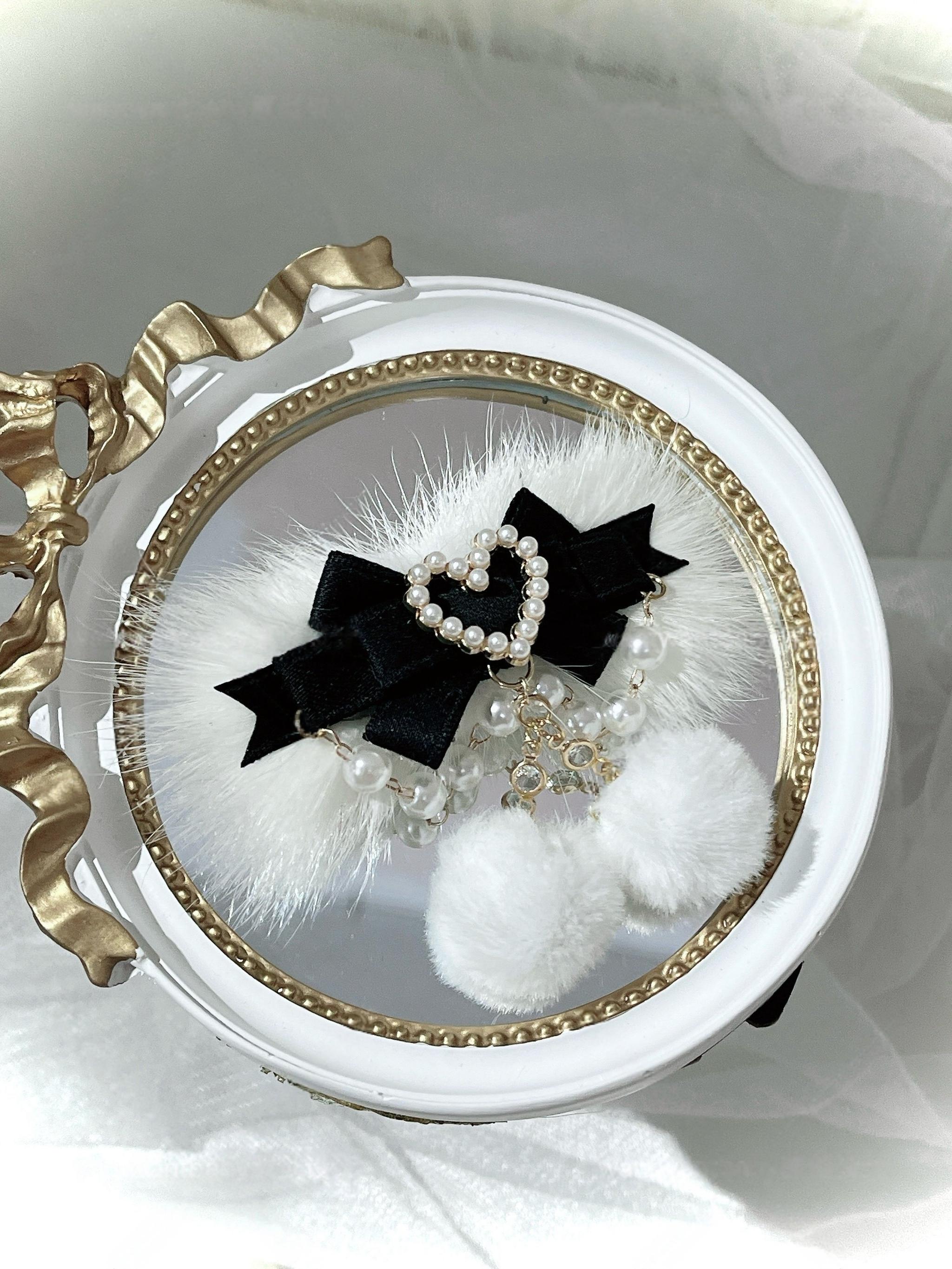 Black velvet ryousangata pom-pom hair clip with white fur trim and pearl heart charm on vintage gold-edged white tray, jirai kei lolita accessory flat lay photography