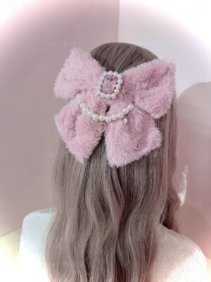 Bean-paste pink fuzzy ryousangata bow hair clip with pink rhinestone gemstone and decorative pearl chain, back view on female model, jirai kei fashion accessory