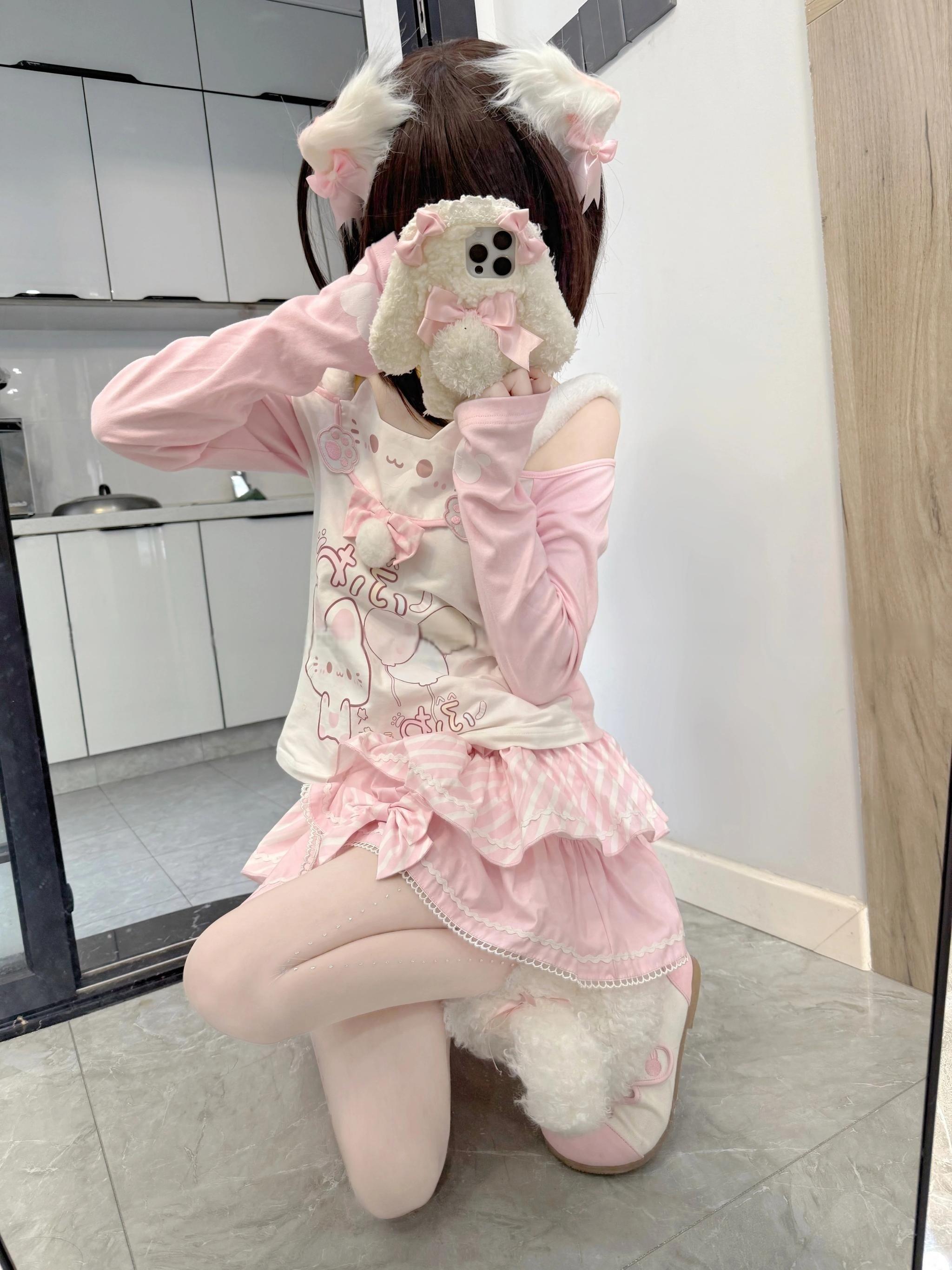 Jirai Kei-inspired cat-themed complete outfit featuring off-shoulder top and pink tiered skirt with white tights, kneeling low-angle pose demonstrating skirt volume and fluffy cat tail accessory coordination