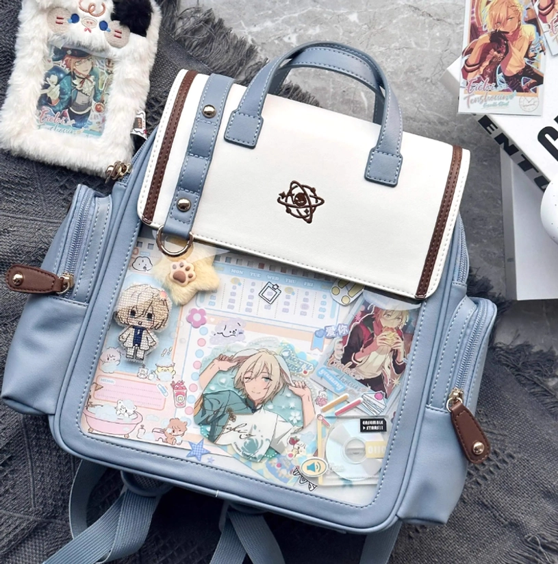 Decorated anime itabag backpack top-down front view with collectible charms and merchandise on fuzzy desktop display