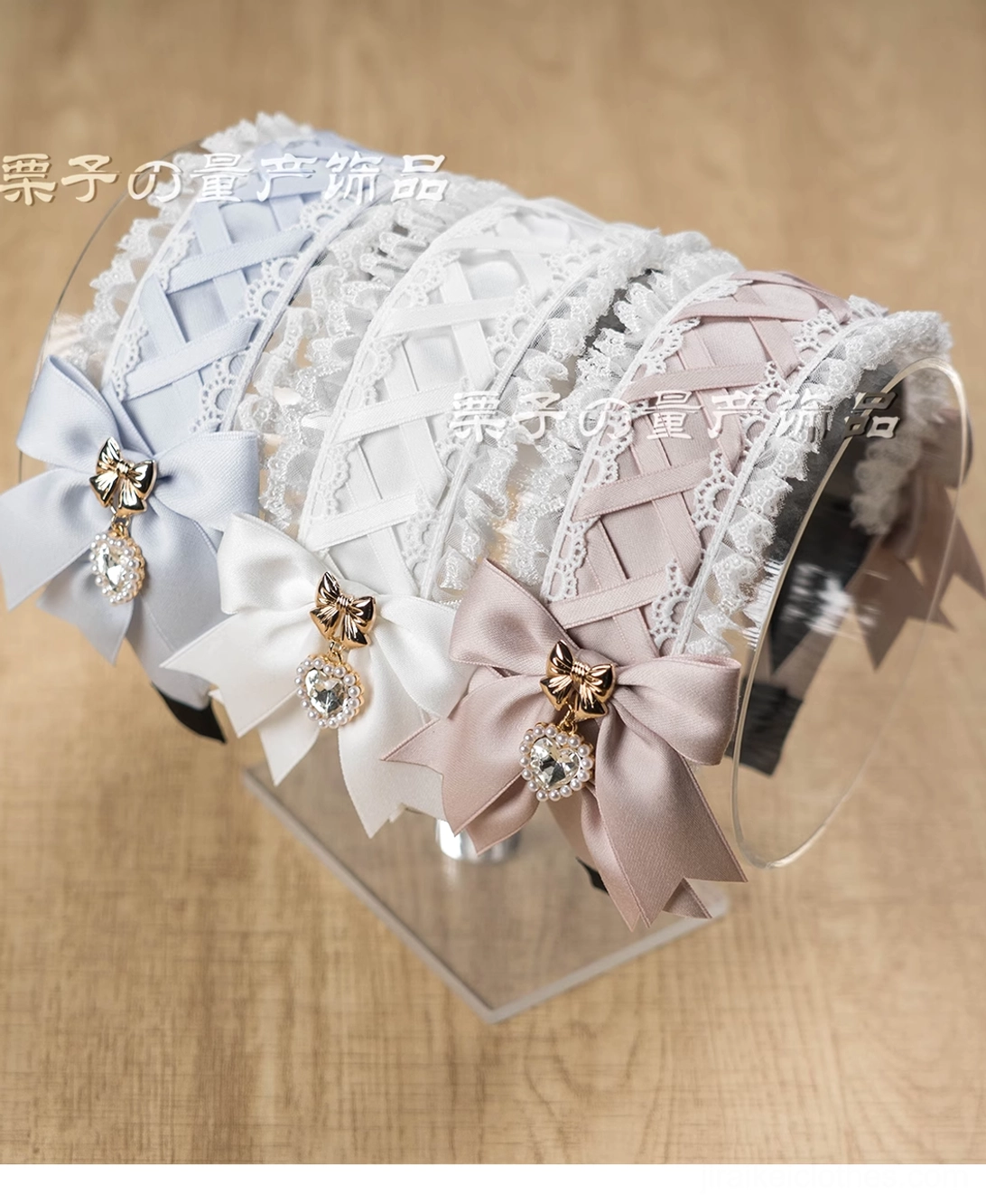 Top-down flat lay of assorted Jirai Kei lace headbands in multiple colors displayed on wooden table with acrylic display stand, showing satin bows with rhinestone pendants and cross-over lace details