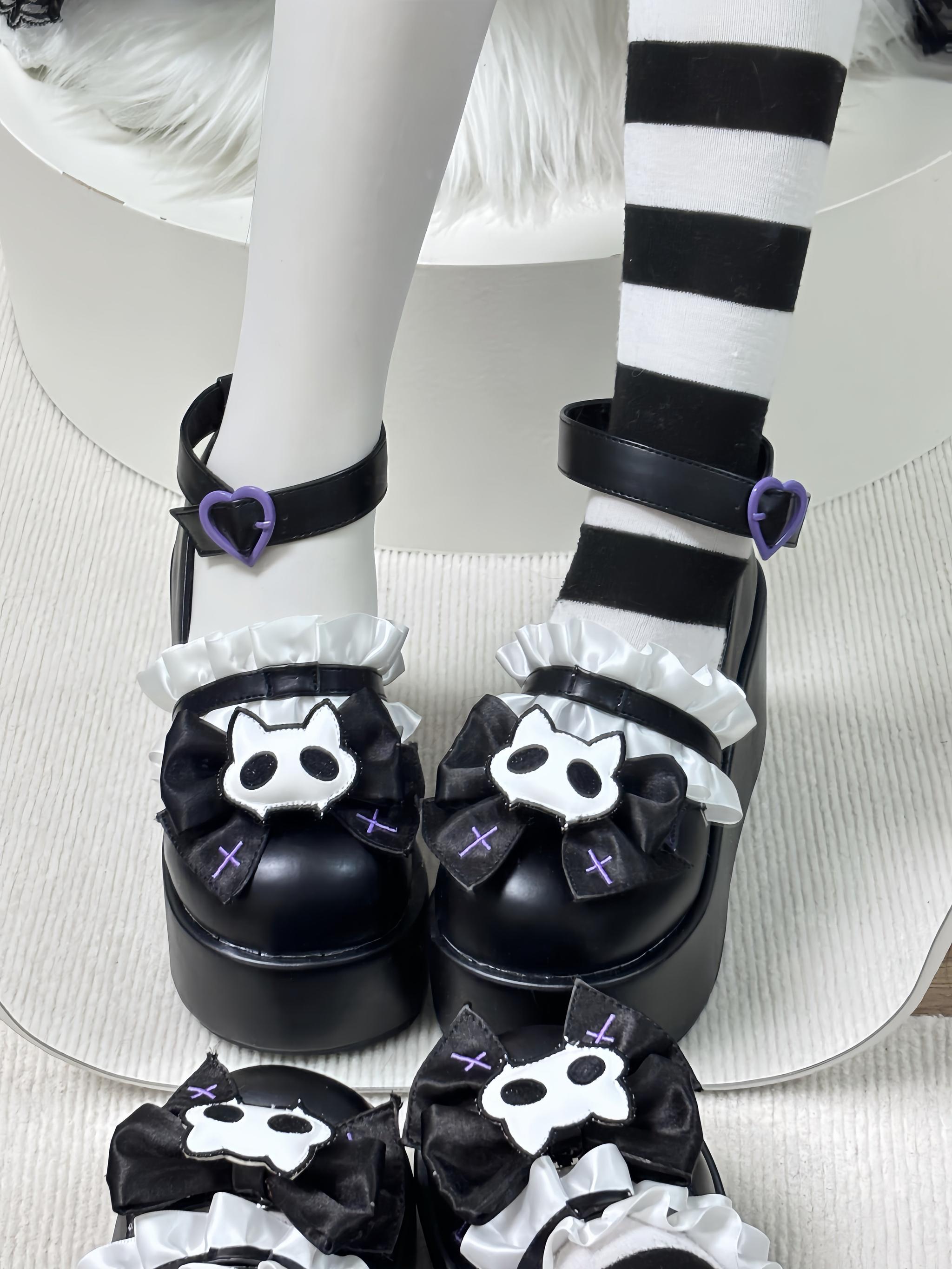 Black gothic platform shoes close up top down view with detachable cat skull bow and purple heart buckle on white fur cushion