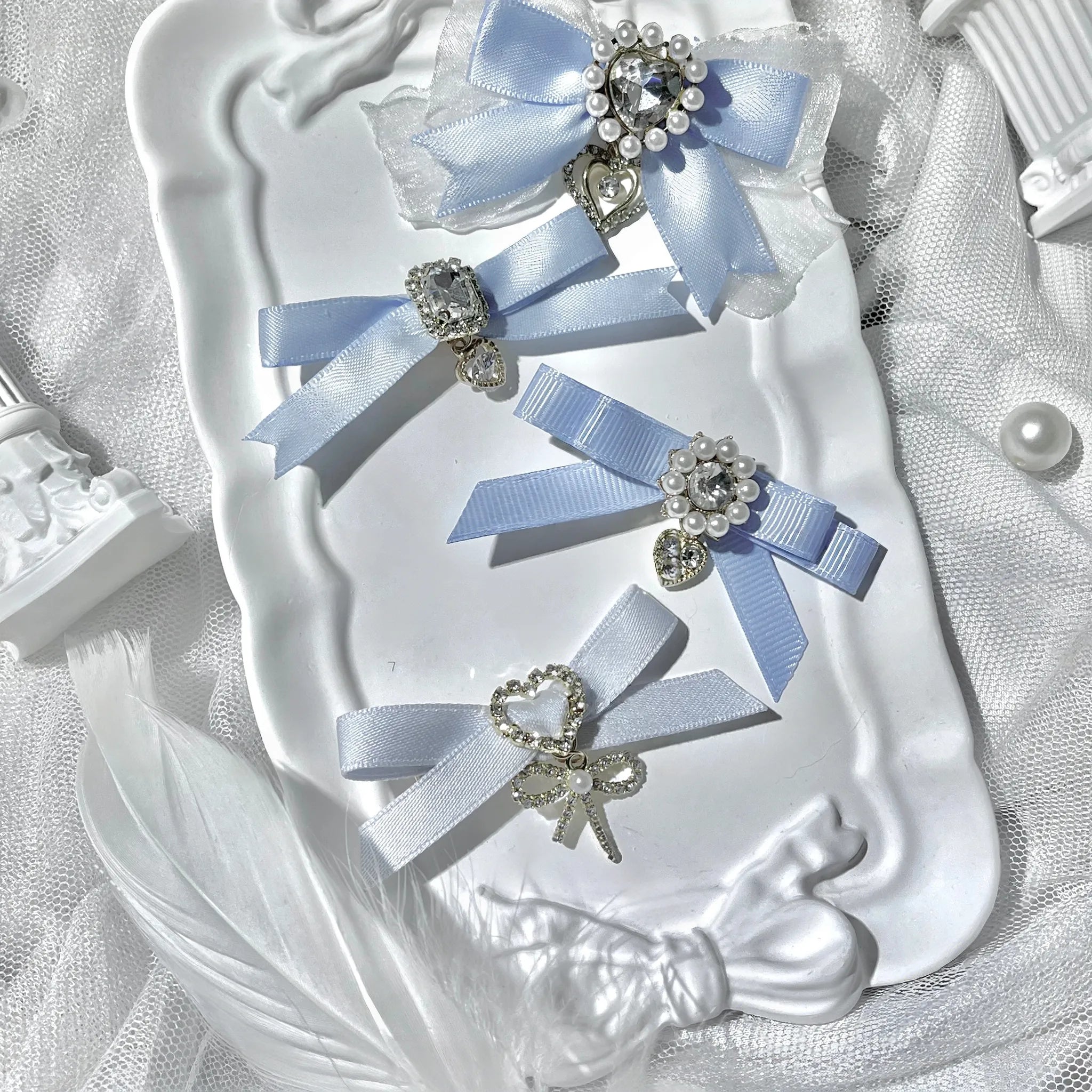 Light blue water blue satin bow hair clips set with rhinestone centers bow and heart pendant decorations on decorative tray lace background flat lay
