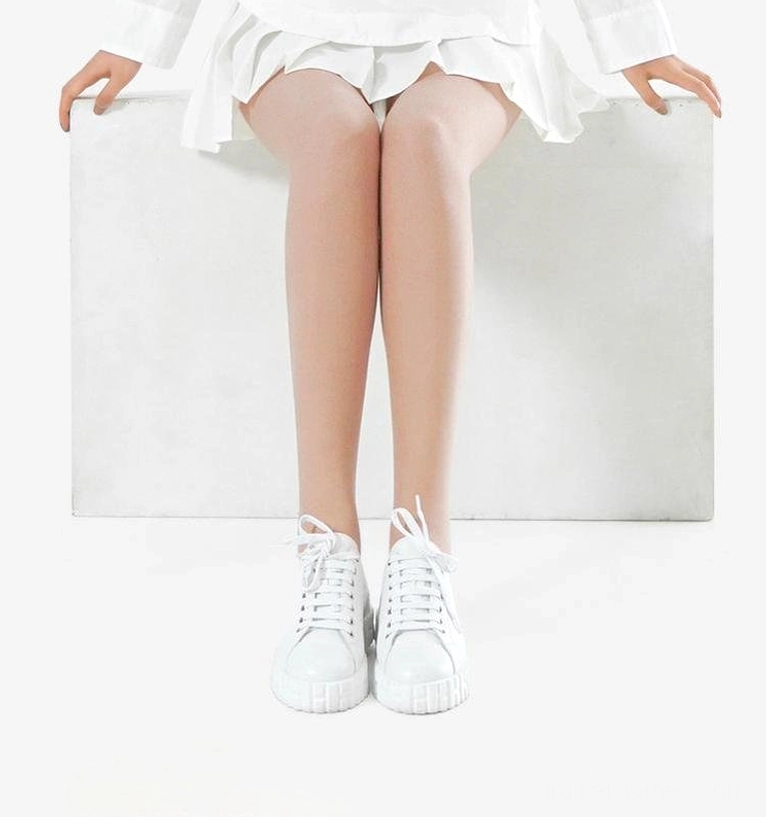 Front seated leg shot of model in beige velvet tights with white outfit and white sneakers - shows smooth unnoticeable leg coverage and modern minimalist styling
