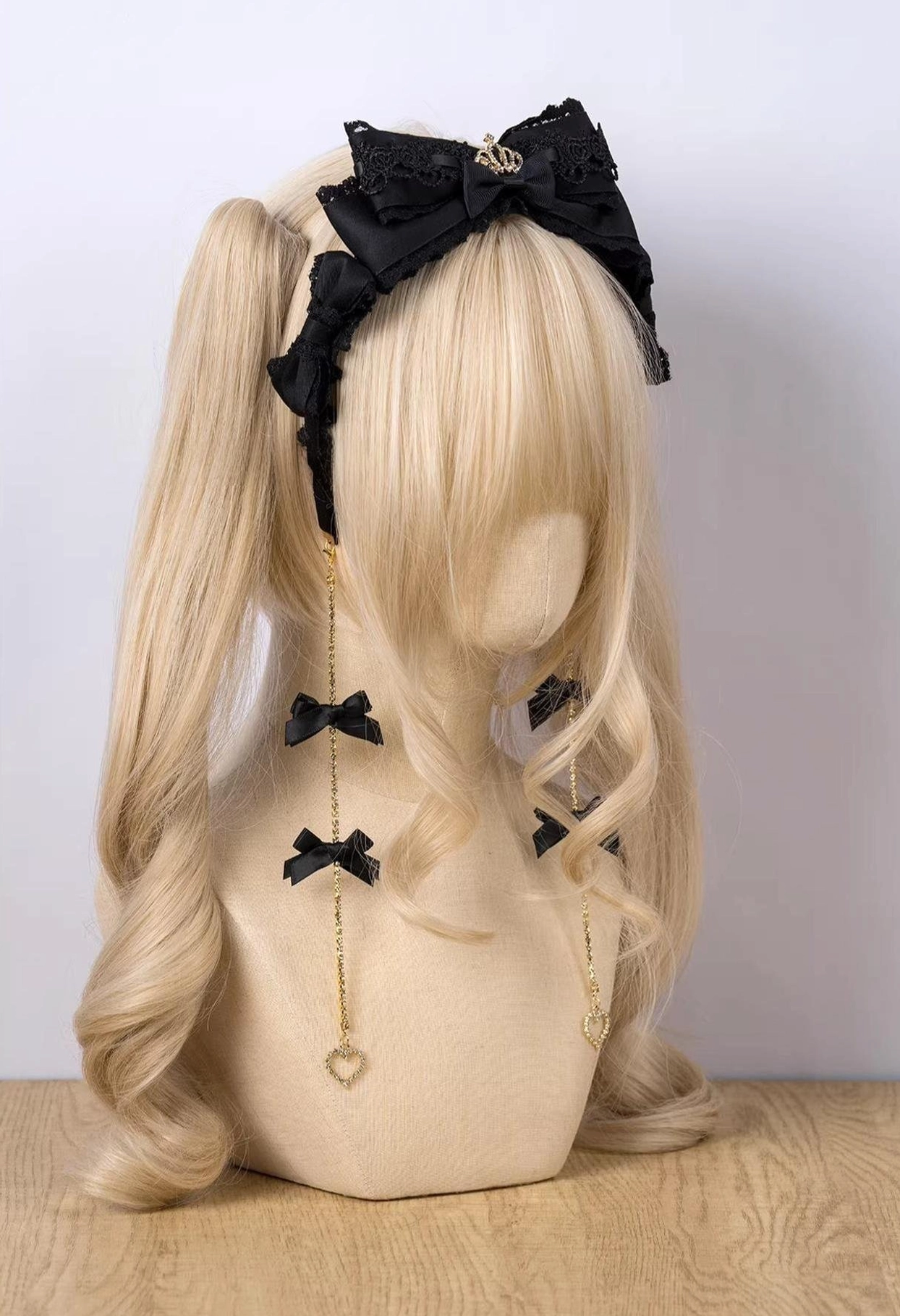 Black bow KC Jirai Kei hair clip with heart-chain dangles on blonde mannequin twin ponytails front view