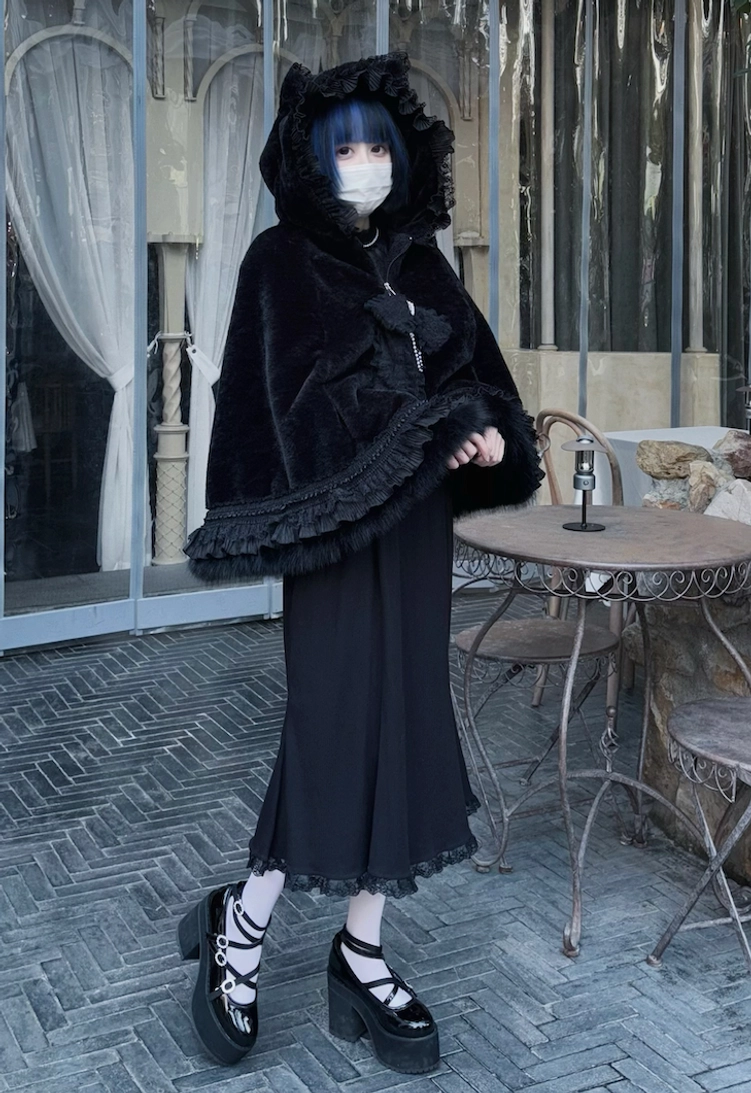 Side three-quarter view of black cat ear hooded fleece cape coat at European style cafe, paired with long lace-trim skirt and platform loafers