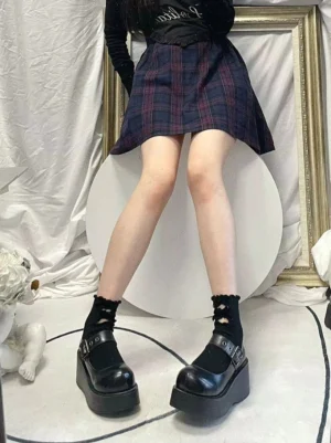 Black platform Mary Jane shoes showcasing thick polyurethane sole and ankle buckle strap, styled with plaid skirt and black patterned crew socks in studio setting with decorative frame