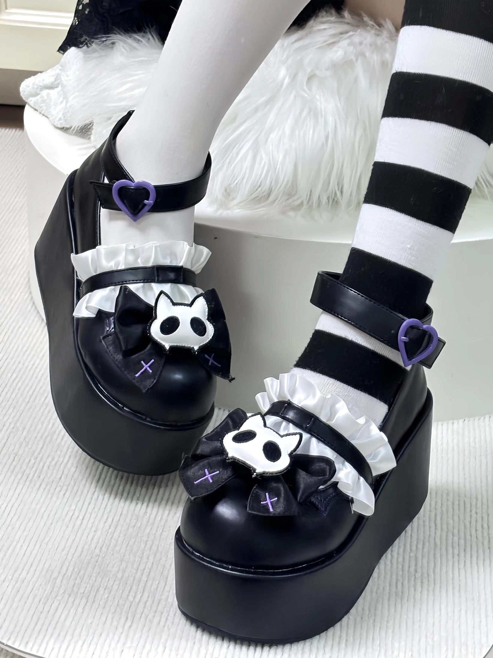 Black gothic platform Mary Jane shoes with purple heart ankle buckle and removable cat skeleton bow side angle view on white fur