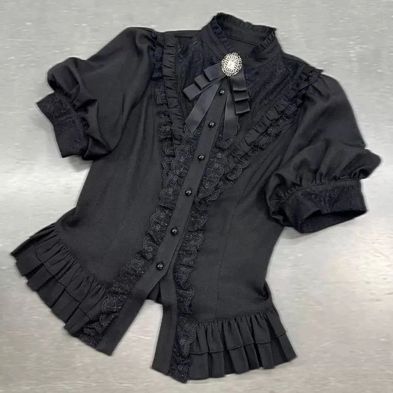 Black gothic puff-sleeve blouse flat lay front view showing stand collar, detachable ribbon bow brooch, front button placket, and ruffled lace trim construction