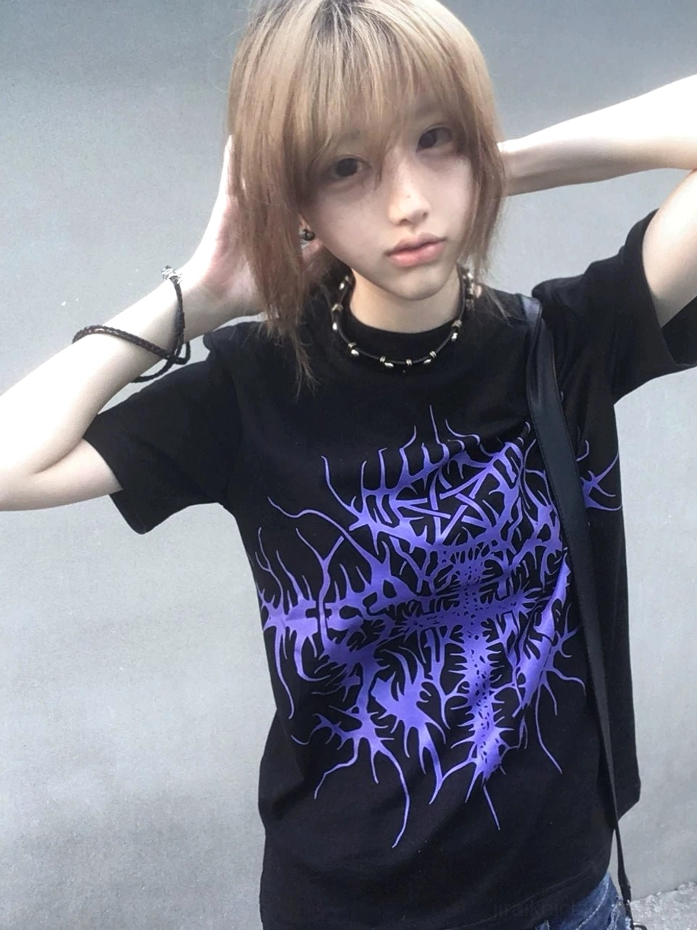 Black gothic t-shirt with large purple thorn cross print on front chest, worn by blonde female model, concrete wall background, dark punk aesthetic