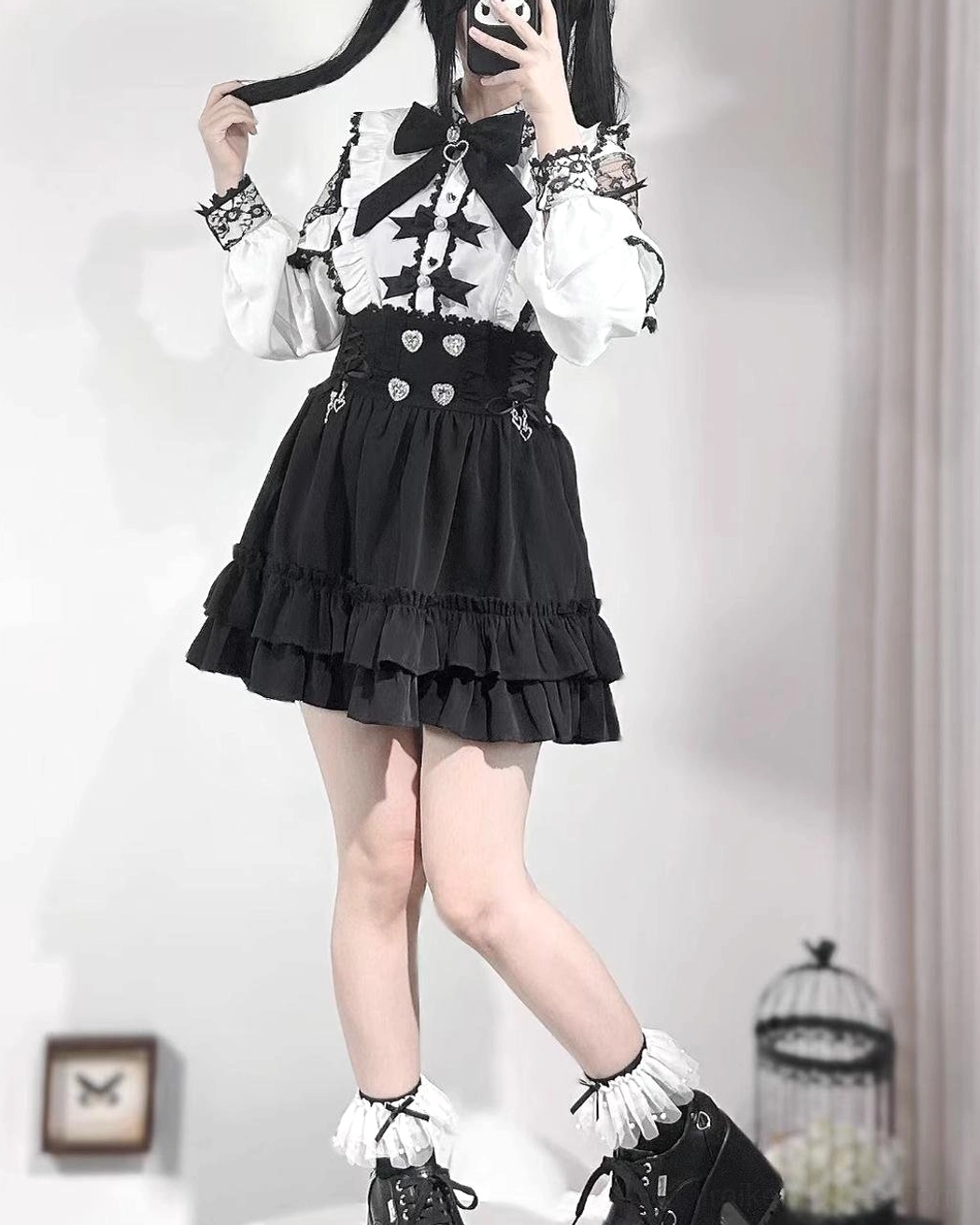 Jirai Kei black A-line skirt back view showing double-layer ruffle hem and lace-trimmed cuffs, model with twin tails taking selfie demonstrating movement of flounce layers
