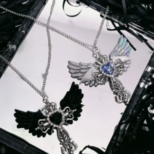 Black Jirai Kei angel wing cross necklace featuring black heart gem and silver metal cross on white tray with dark shredded filler
