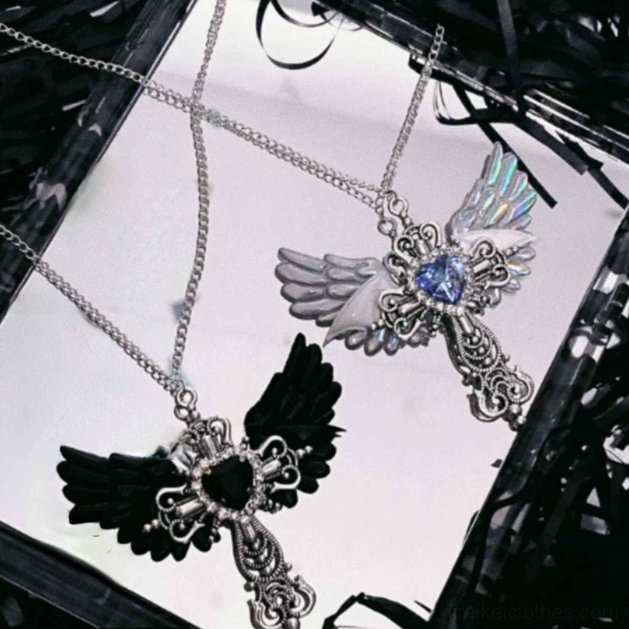 Black Jirai Kei angel wing cross necklace featuring black heart gem and silver metal cross on white tray with dark shredded filler