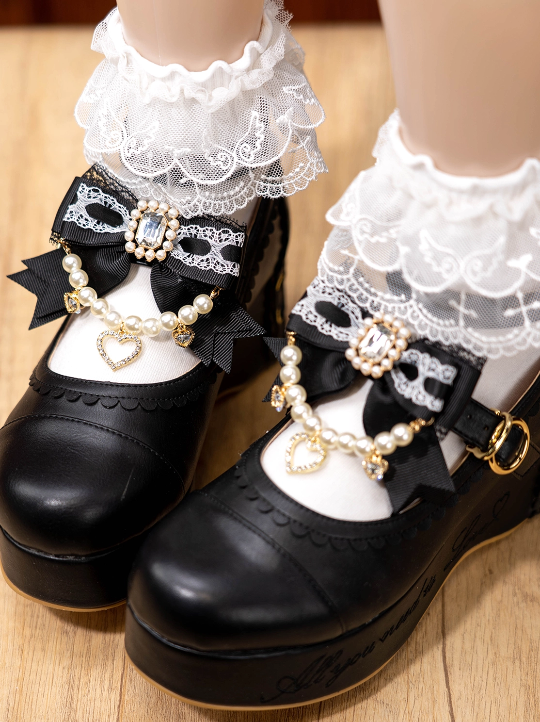 Black bow shoe clips pair with pearl chain and rhinestone details on mannequin feet wearing black Mary Janes lace socks