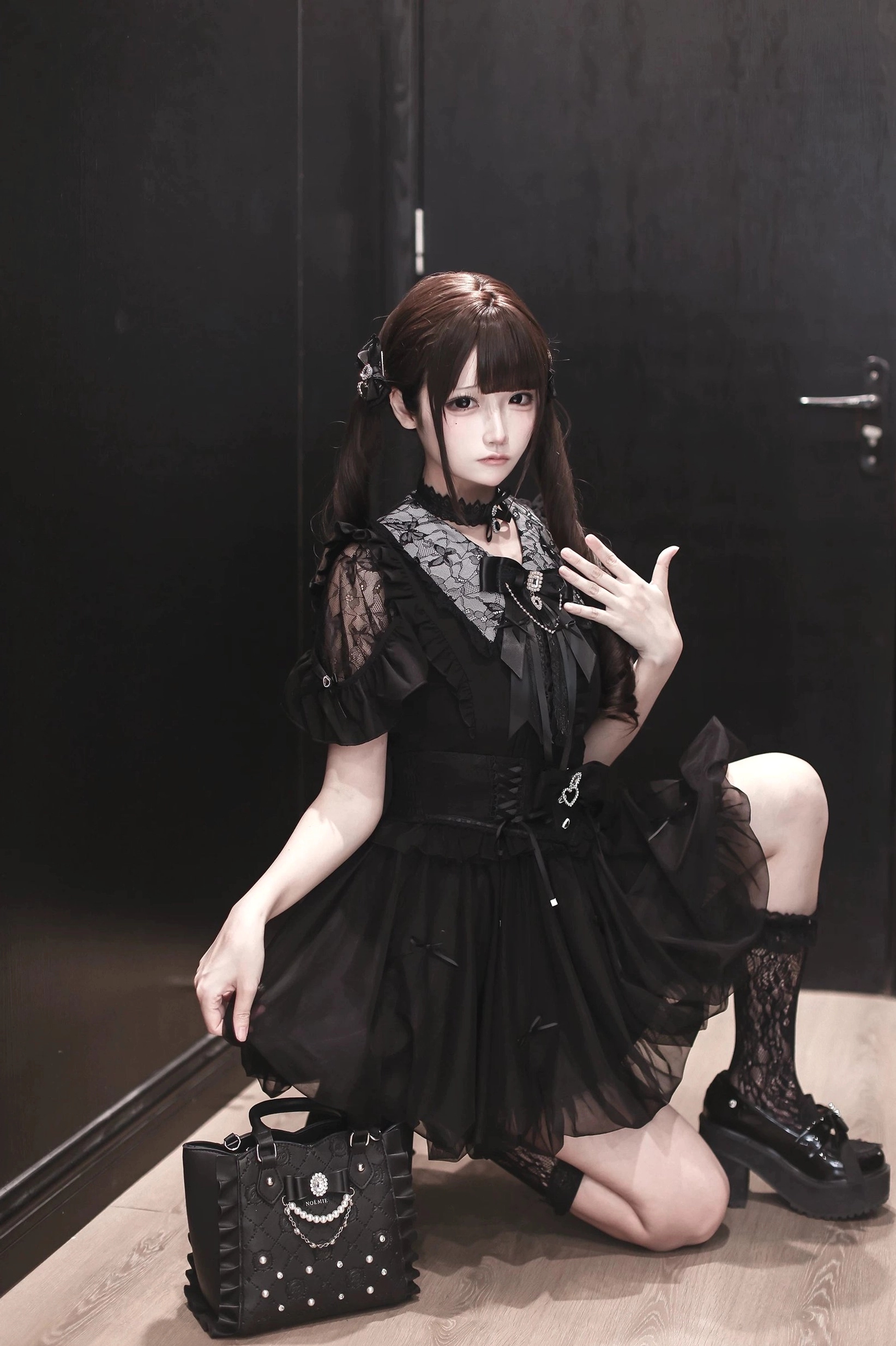 Black Jirai Kei bubble dress with sheer lace sleeves, rhinestone decorations on tulle skirt and matching studded handbag, model kneeling low-angle shot