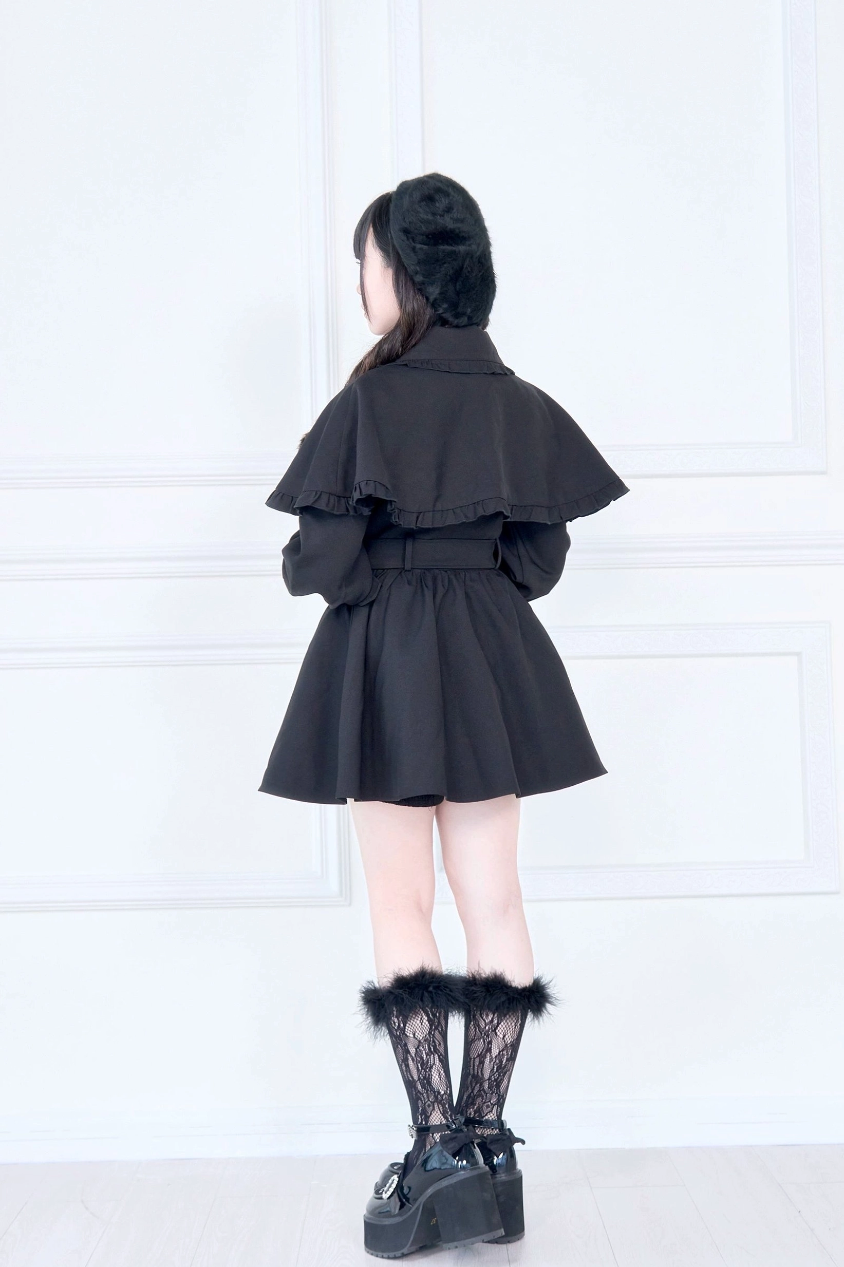 Black cape trench coat back view showing fitted flared pleated skirt hem lace accents and ruffled cape cuffs on model